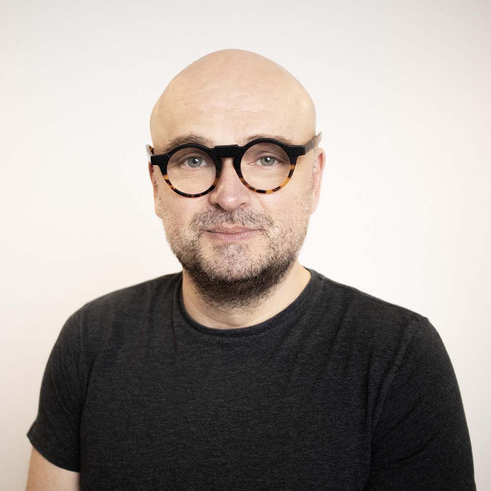 Headshot of a smiling bald headed man with glasses